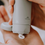 Person pressar ut en liten mängd body lotion från Cana Care i handflatan från en ljusgrön tub.