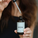 Person håller hårserumet “Grow” från Cana Care och lyfter pipetten med en droppe serum över flaskan.