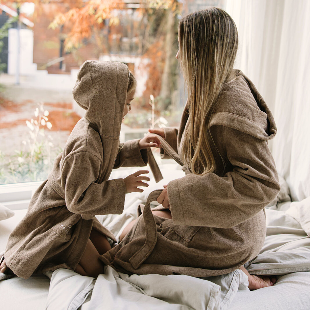 Barn och mamma i matchande bruna morgonrockar leker vid fönstret med höstutsikt.